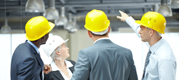 Business people in hard hats looking at ceiling, one person pointing