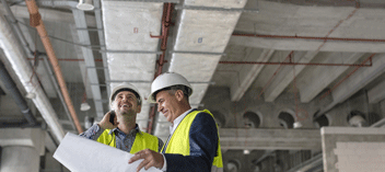 Two business men in hard hats reviewing plans in interior of building