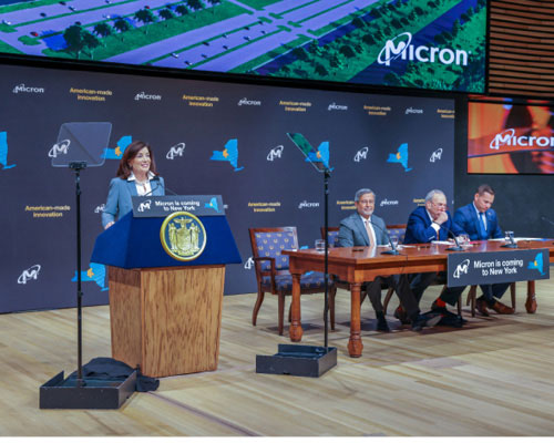 Govenor Kathy Hochul speaking at a podium next to table with "Micron is coming to NY" sign.