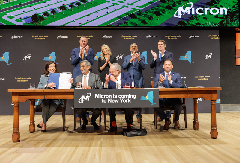 Business panel at a table with "Micron is Coming to New York" sign.