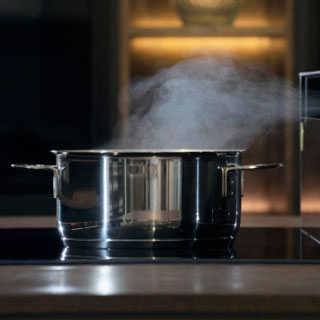 A pot on a cooktop with steam coming out the top.