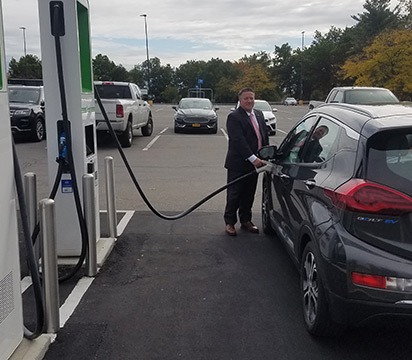 County Executive McCoy charging an electric car at a station outdoors.