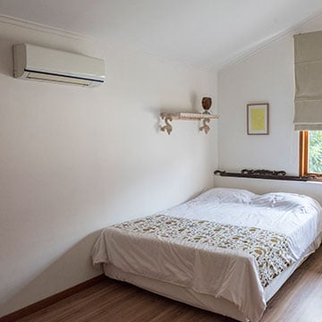 An all white bedroom with a bed in the corner and a mini split on the wall.