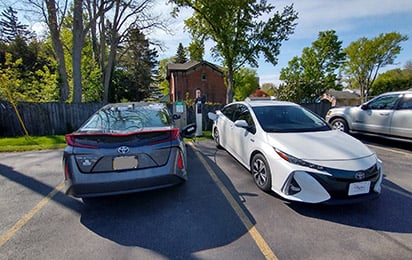 Two cars plugged into an EV charging station in an outdoor parking lot.