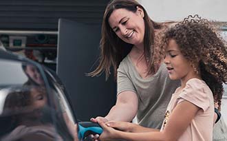 Closeup of a woman helping a young girl plug in an electric vehicle.