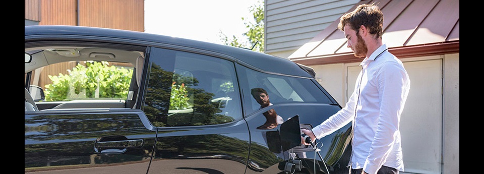 Closeup of a man plugging in an electric vehicle in his driveway.