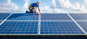 Worker in a safety hat and harness installing a rooftop solar panel.
