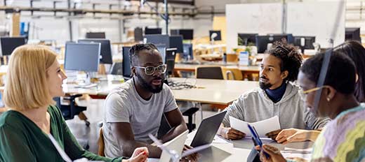 People meeting around a table with open concept office space in background.