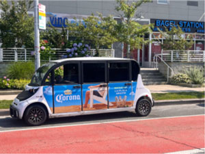 A small transport van with a Corona advertizing wrap outside a building.