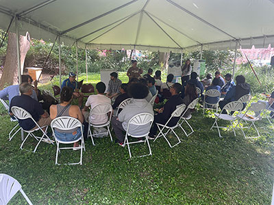 Two groups of people sitting in lawn chairs under a tent participating in the Kreuger event.