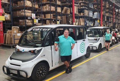 Two drivers standing next to electric vehicles inside a warehouse.