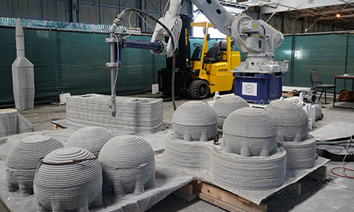 3D printed concrete forms with concrete printer in background.