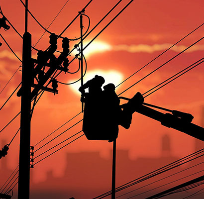 Silhouette of lineworkers in bucket with bright sun and orange sky in the background.