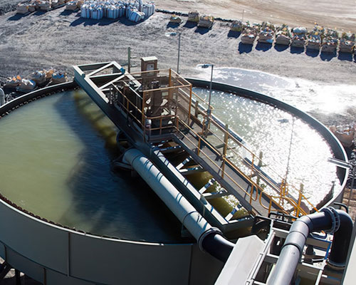 Large circular industrial tanks filled with liquid, connected by pipes and walkways at a processing site.