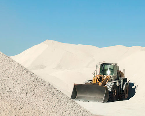 Front loader moving mineral piles under a clear blue sky.