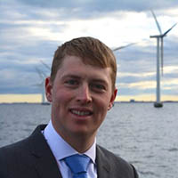 Portrait of man smiling with sea and wind turbine in the background. 