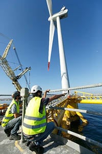 Offshore wind workers in hard hats prepare to service an offshore wind turbine.