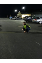 Image of man crouching and inspecting the area, streetlight in the background. 