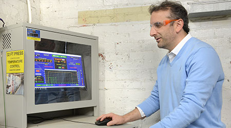 Man with safety glasses on standing at a computer monitoring station.