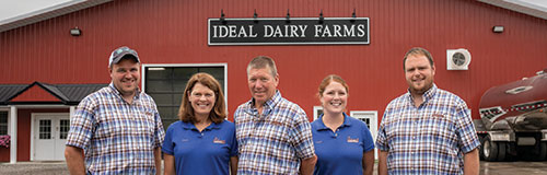 Five members of the Ideal Dairy Farms family posing in front of the red barn.