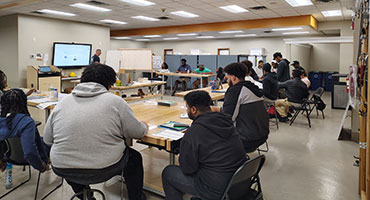 People seated around SEAT Center classroom and a presenter in front of a projector screen.