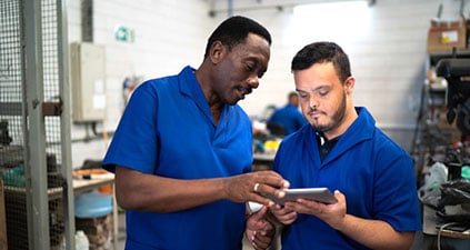 Two people in blue shirts looking at a data pad.