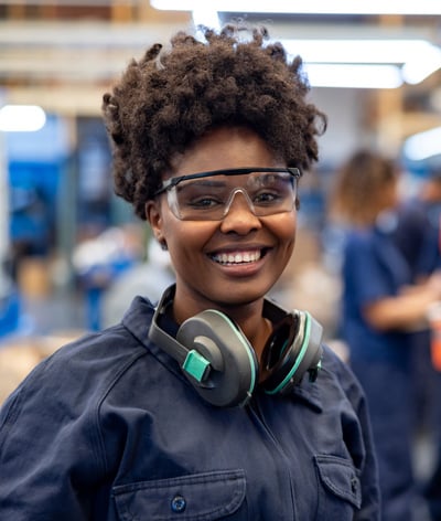 A woman wearing safety glasses and carrying safety earmuffs around her neck.