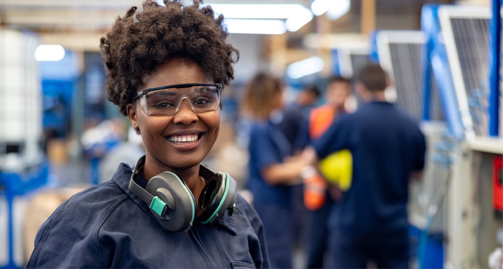 A woman wearing safety glasses and carrying safety earmuffs around her neck.