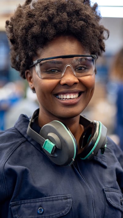 A woman wearing safety glasses and carrying safety earmuffs around her neck.