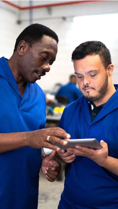 Two people in blue shirts looking at a data pad.