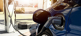 Close up image of a charger plugged into an EV -or- image of an “EV Parking Only” sign