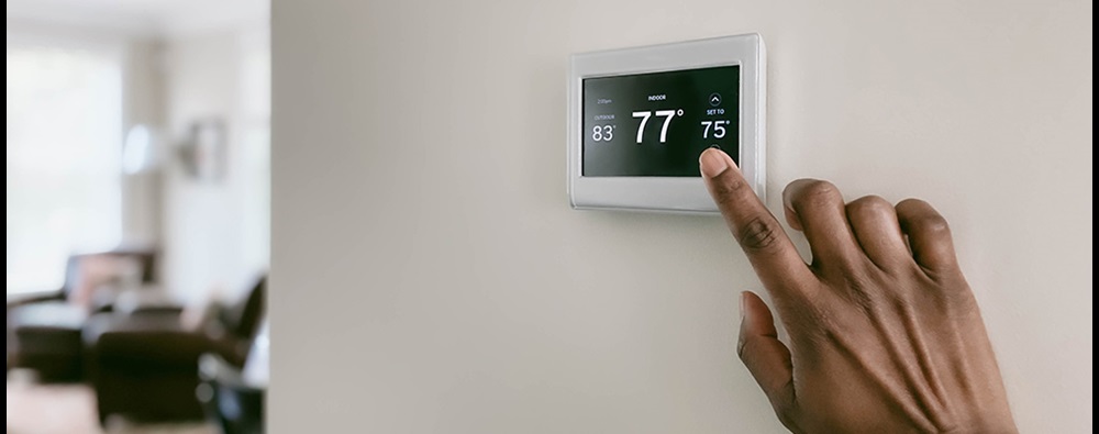 A digital thermostat mounted on a wall and a hand moving to press the display.