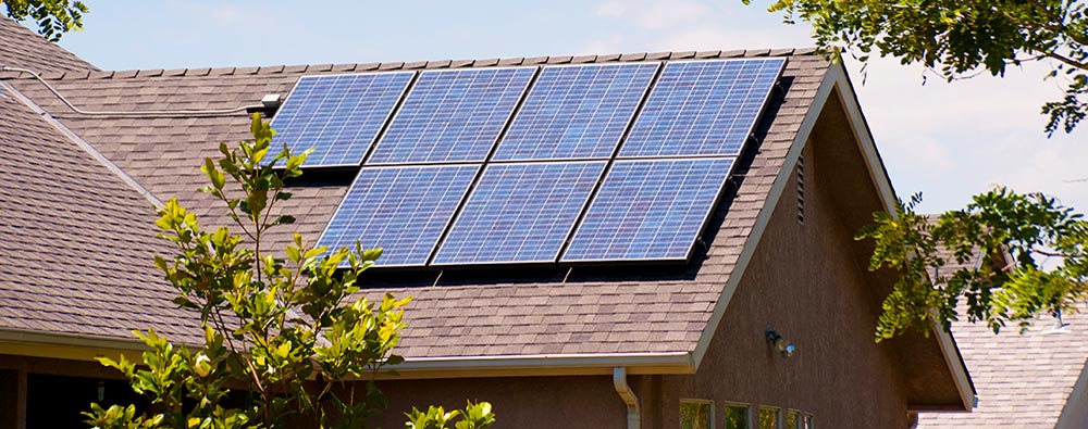 Solar panels mounted on the roof of a house with brown shingles.