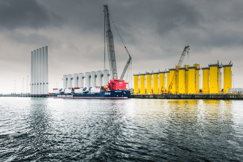 Large offshore wind components being loaded onto a vessel at a port facility.